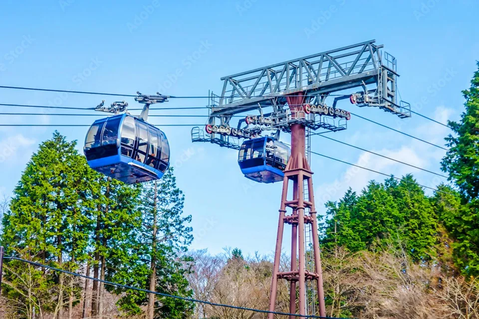 Hakone Komagatake Ropeway gondolas against a backdrop of trees and blue sky.