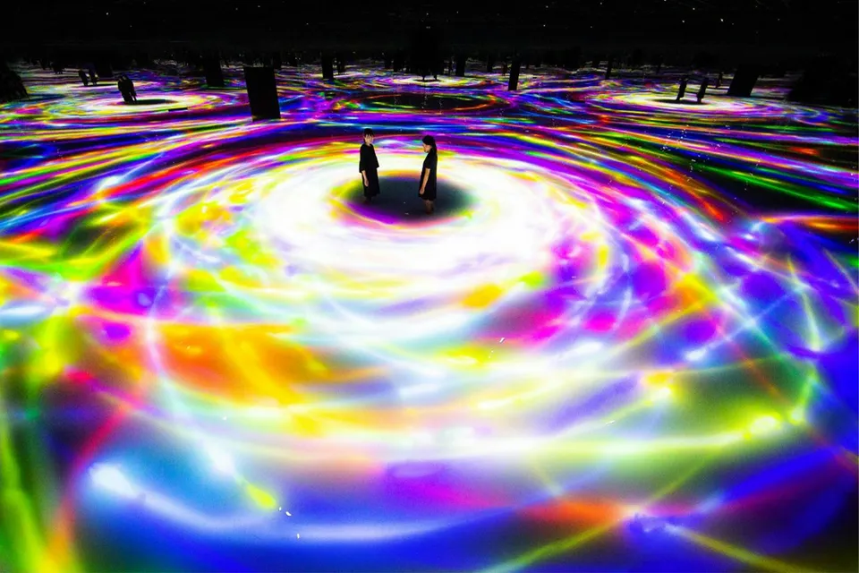 Visitors at TeamLab Planets Tokyo surrounded by swirling colorful digital light displays.