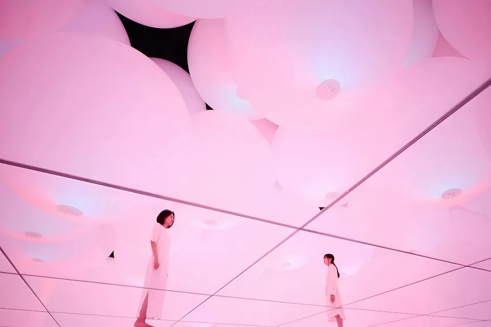 Visitors in mirrored room with pink digital light at TeamLab Planets Tokyo exhibit.