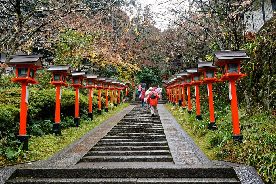 Steps lined with red lanterns leading to Kinkaku-ji temple, people walking up.
