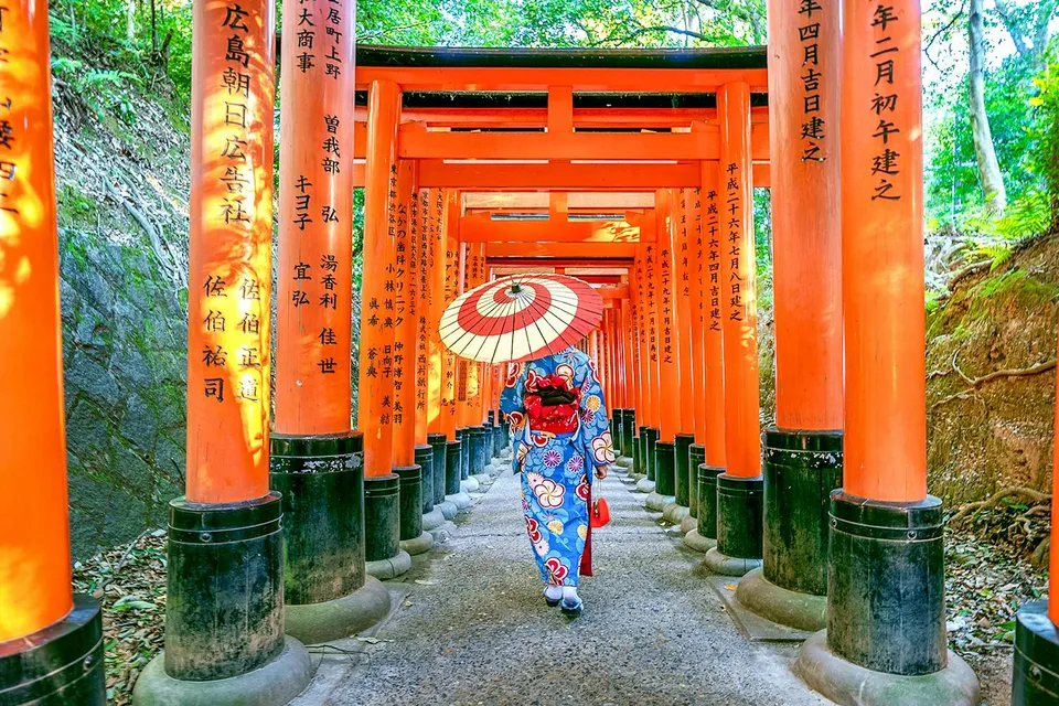 Person in kimono walking through Fushimi Inari Shrine's torii gates, Kyoto.