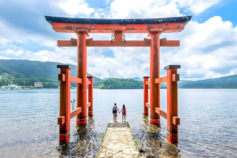 Couple standing at Hakone Torii Gate overlooking Lake Ashi, Japan.