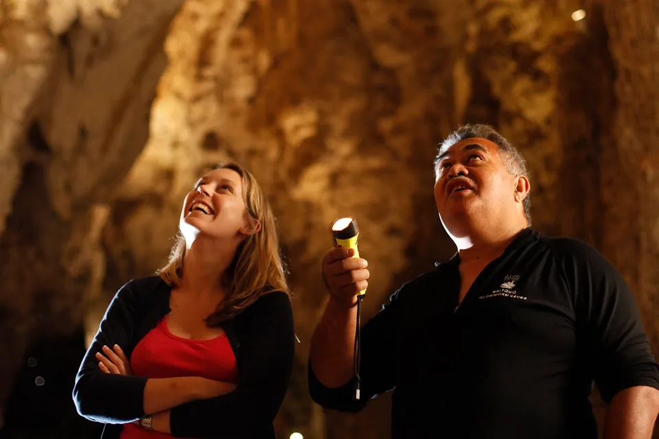 Visitors exploring Waitomo Glowworm Caves with a guide holding a flashlight.