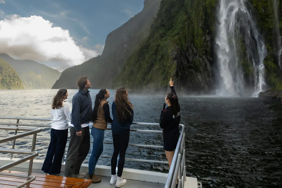 Tourists on a boat admire a waterfall at Milford Sound, New Zealand.