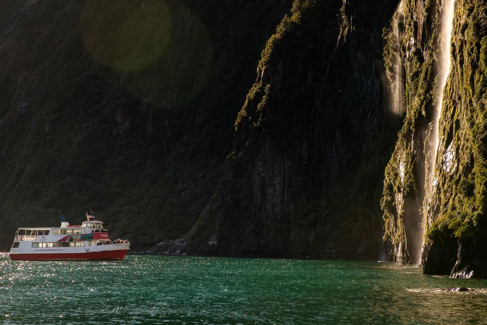 Cruise boat near waterfall in Milford Sound, New Zealand.