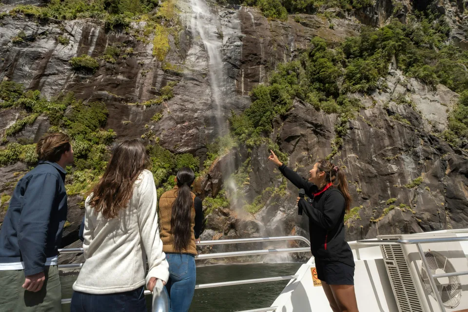 Tourists on a boat admire a waterfall at Milford Sound, New Zealand.