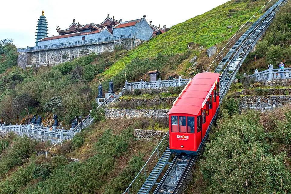 Red funicular ascending Fansipan Mountain with pagoda in background at Sun World Fansipan Legend, Vietnam.