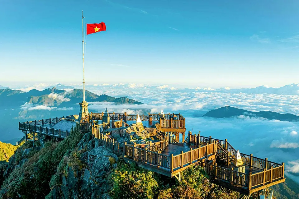 Viewing platform at Sun World Fansipan Legend with Vietnam flag, surrounded by clouds and mountains.