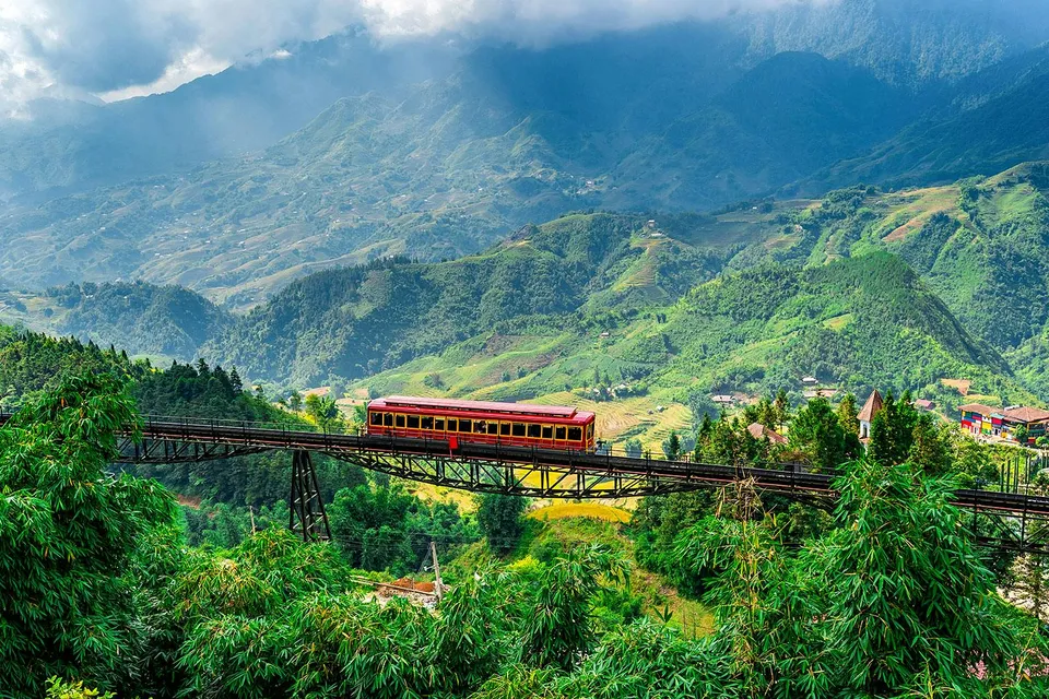 Red train crossing a bridge with Fansipan mountain landscape at Sun World Fansipan Legend, Vietnam.