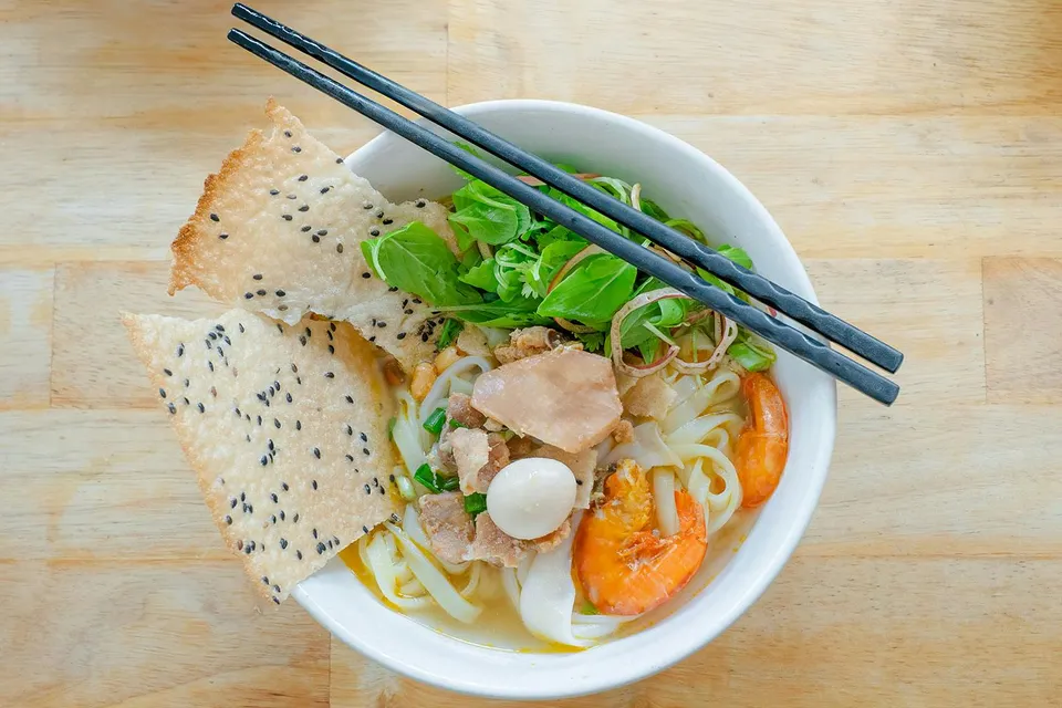 Vietnamese rice noodles with shrimp, herbs, and sesame crackers in a bowl.
