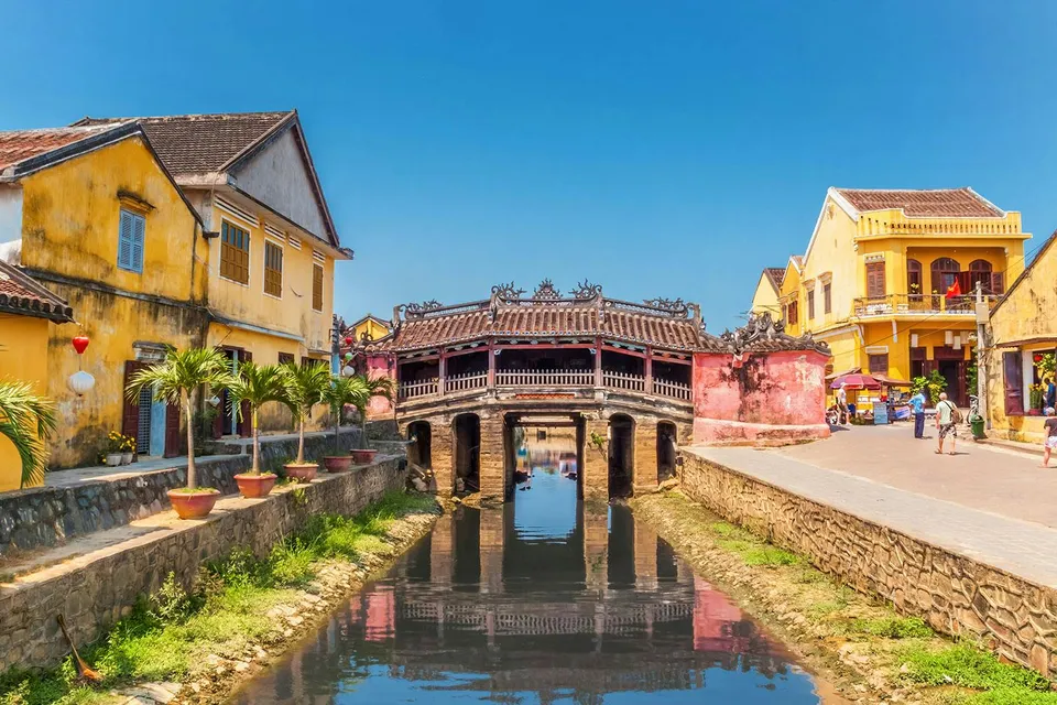 Japanese Covered Bridge over canal in Hoi An, Vietnam, with yellow buildings nearby.