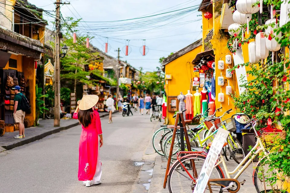 Street scene in Hoi An Ancient Town, Vietnam, with a woman in traditional dress and colorful shops.