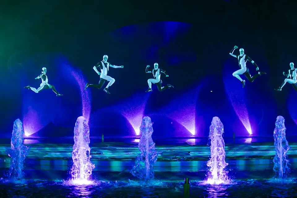 Performers in mid-air during the Kiss of the Sea Show with illuminated fountains.