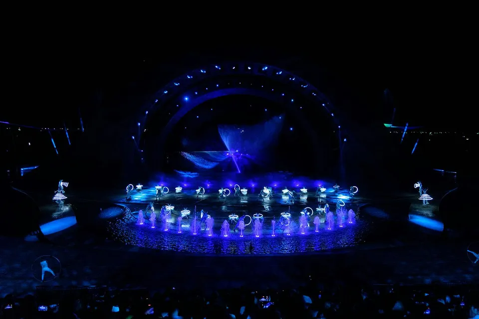 Performers with glowing props in a water-themed stage show, Kiss of the Sea.