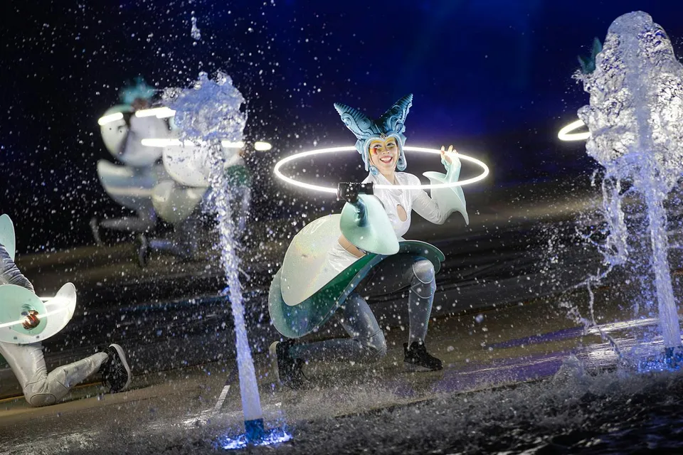 Performer with glowing hoop at Kiss of the Sea Show, surrounded by water fountains.