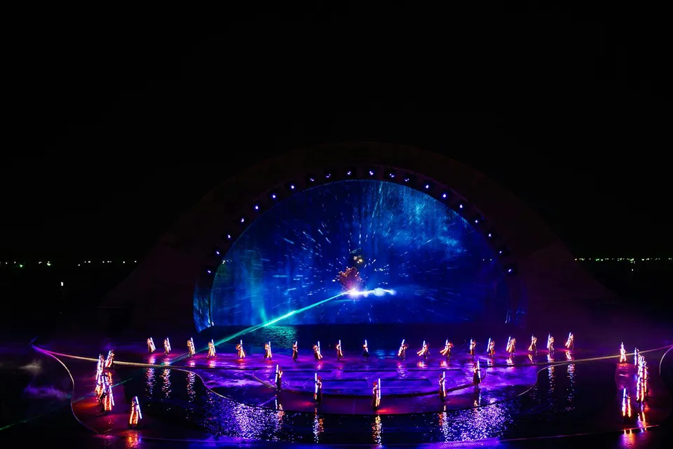 Performers in illuminated costumes at the Kiss of the Sea Show with vibrant water and light display.