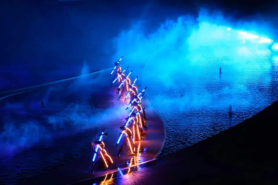 Performers with illuminated costumes in a blue-lit water stage at Kiss of the Sea Show.