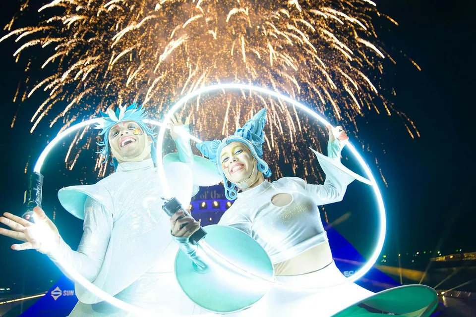 Performers with glowing hoops at Kiss of the Sea Show, fireworks in the background.