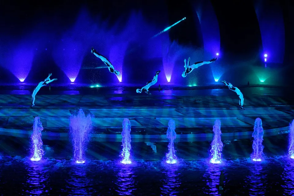 Acrobats performing mid-air flips over illuminated fountains at the Kiss of the Sea Show.