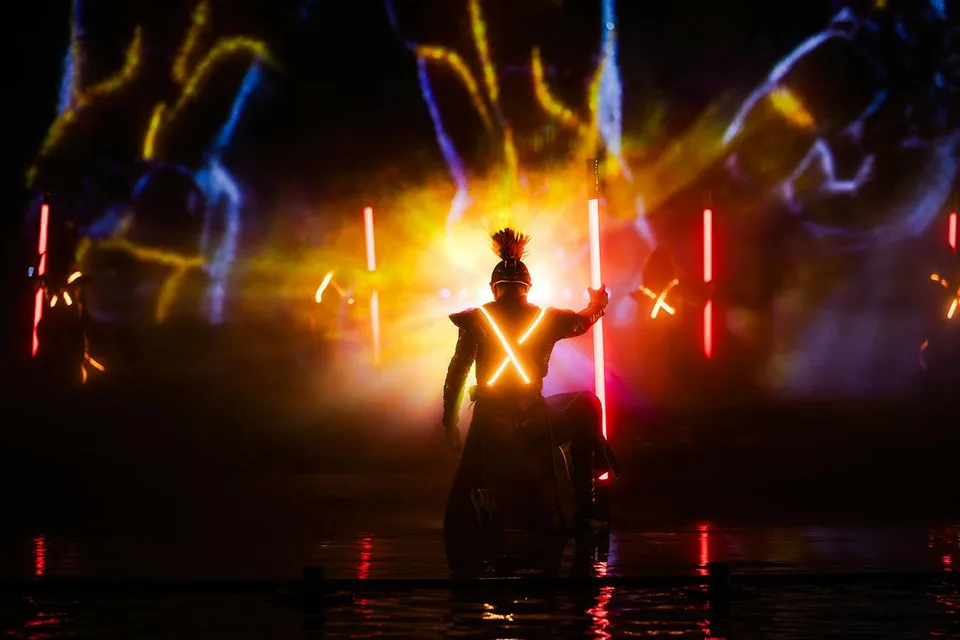 Performer in illuminated costume during Kiss of the Sea Show with vibrant lights.