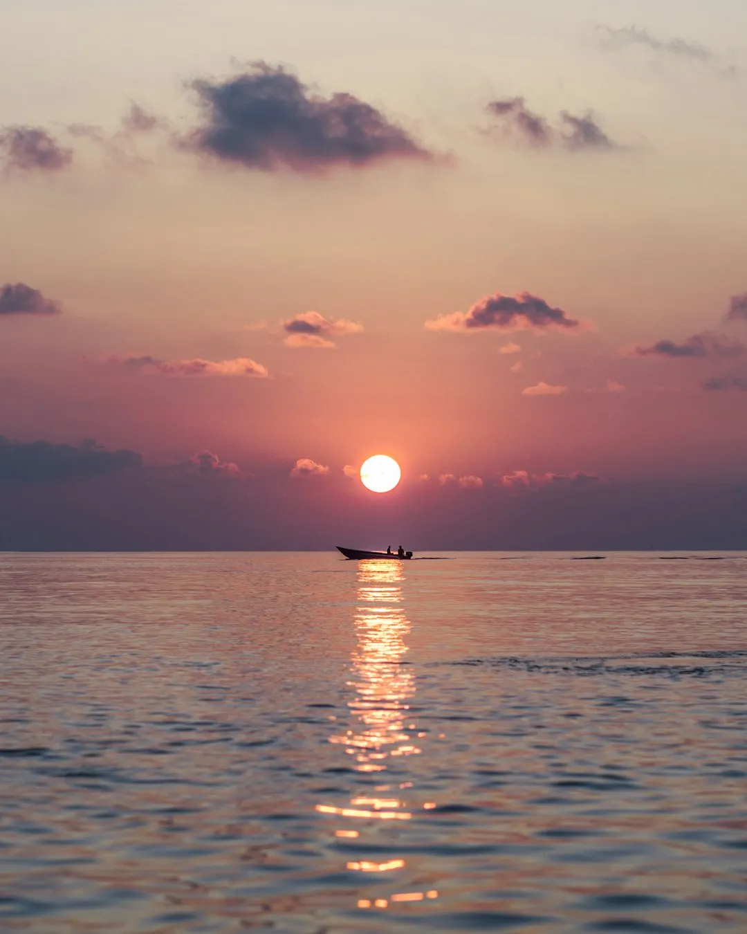 A small boat on calm water under a warm orange sky at low sun