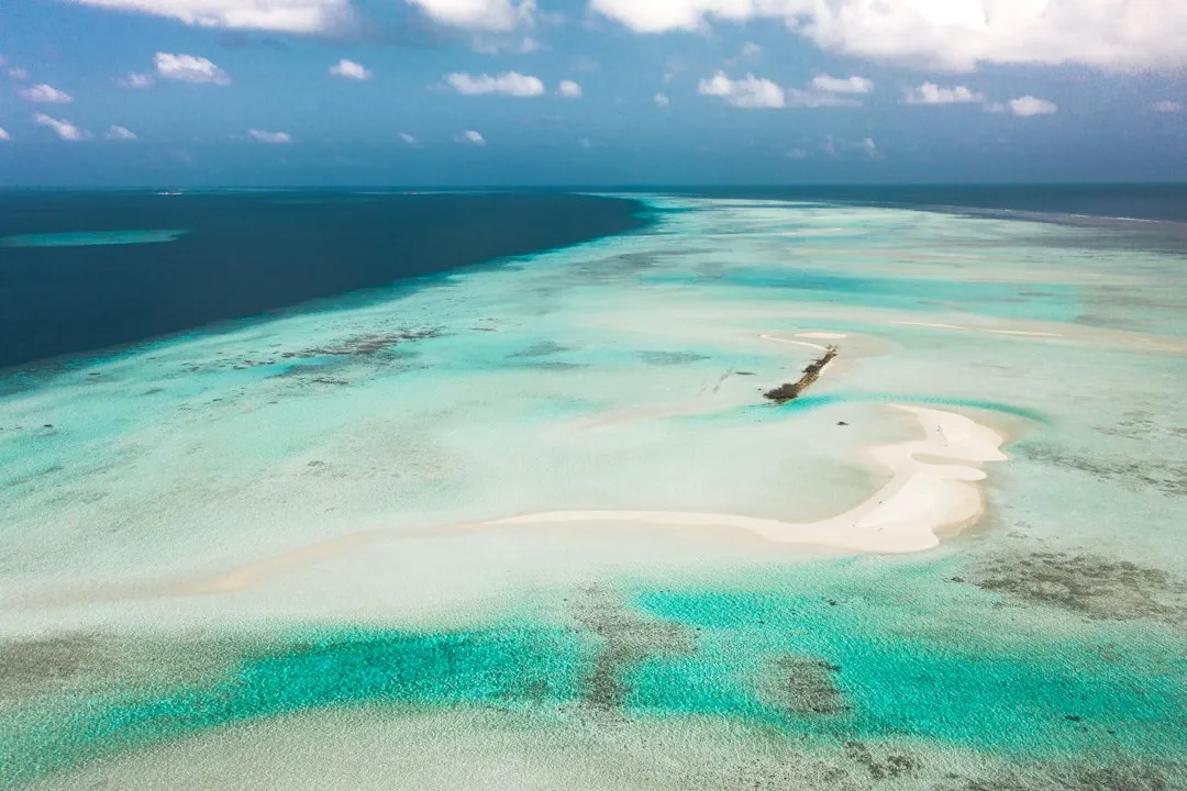 An aerial view of a white sandbar in turquoise tropical water