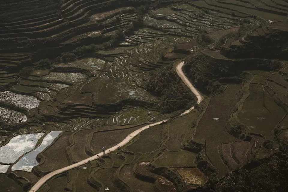A winding dirt road through terraced rice paddies in a mountainous landscape