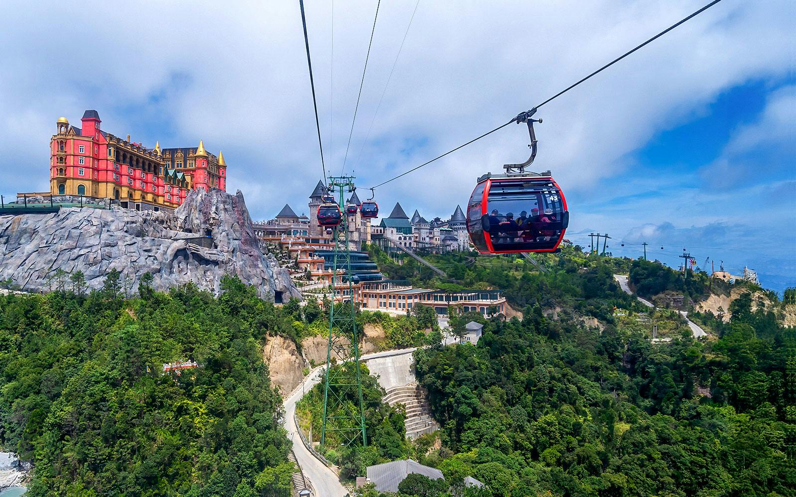 Cable car ascending to Ba Na Hills with scenic view of lush landscape and hilltop buildings.