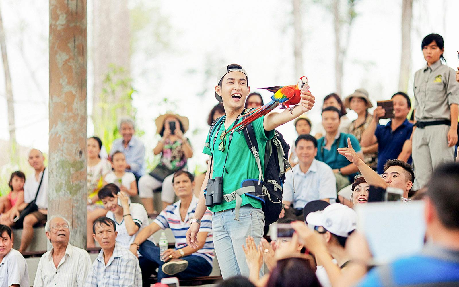 Man holding a colorful parrot during a bird show at Vinpearl, with an audience watching.