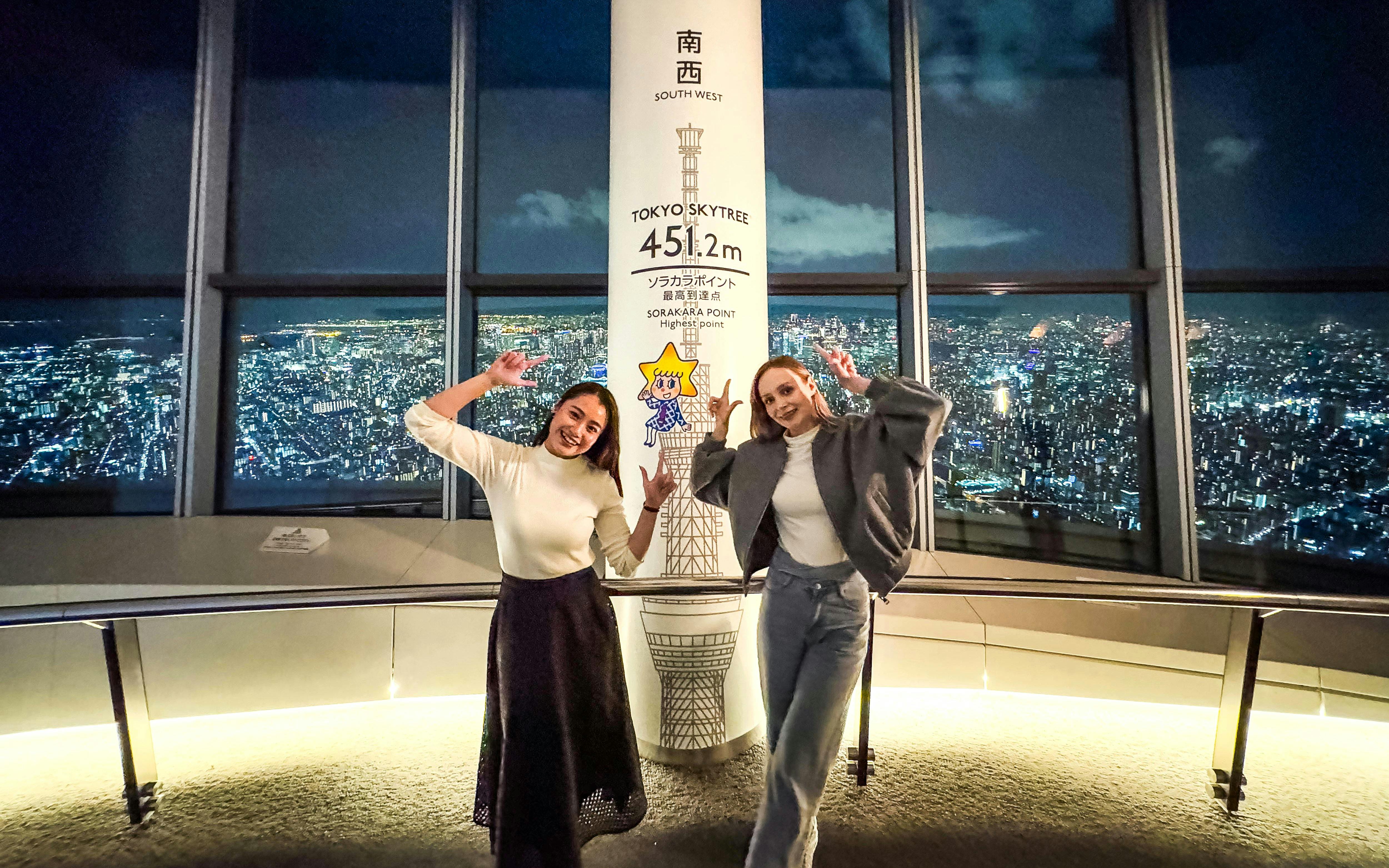 Visitors at Tokyo Skytree's observation deck with city view at night.