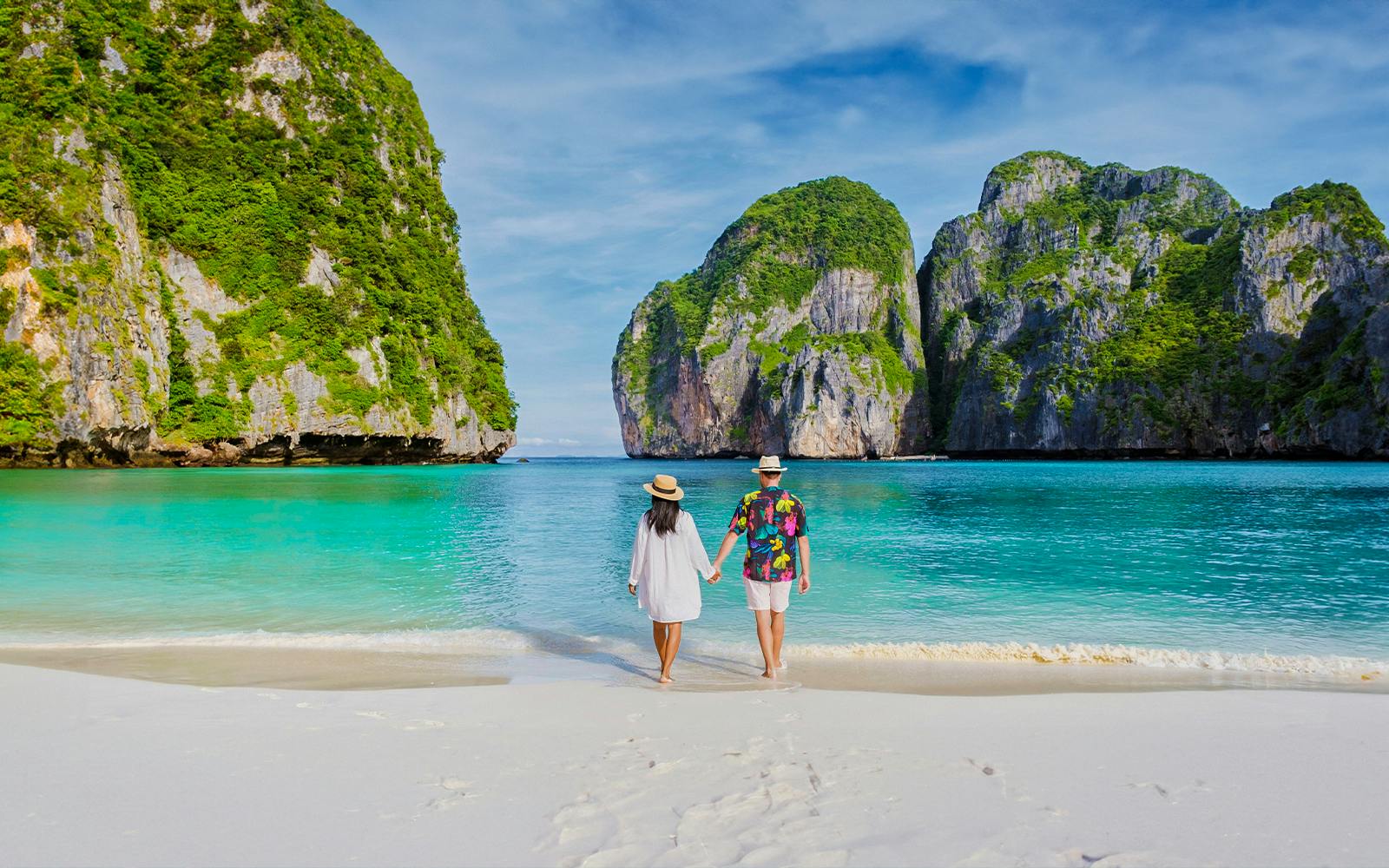 Couple walking on Phi Phi Island beach with limestone cliffs in background.