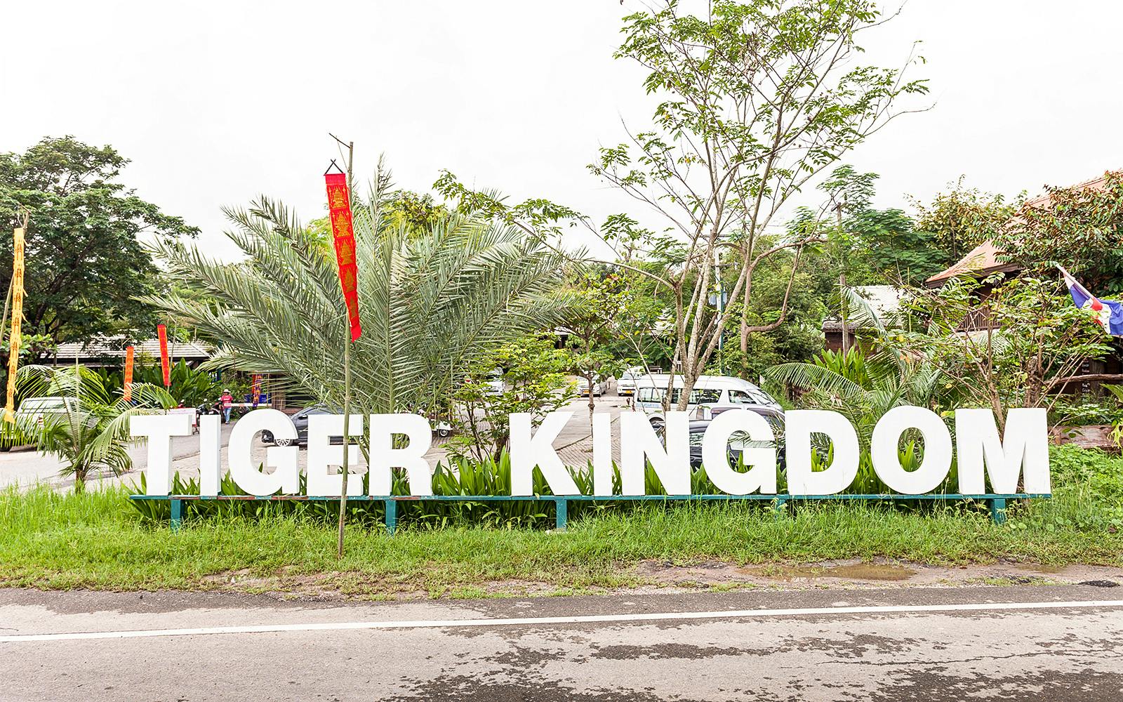 Tiger Kingdom entrance sign surrounded by greenery and flags.