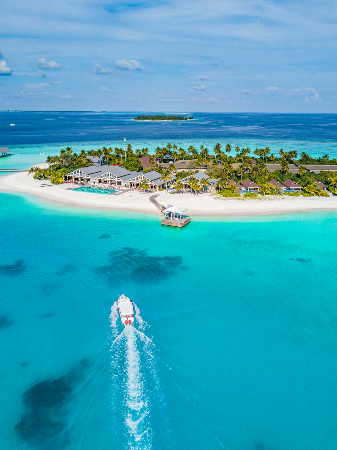 A boat traveling through turquoise water toward a tropical island resort in the Maldives
